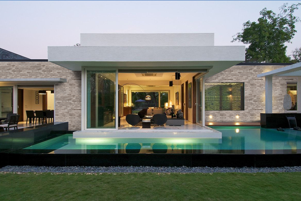 A modern house with a pool out the front. Glass bifold doors leading out to the pool and the house is made from light coloured bricks