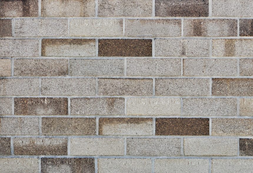 A wall constructed with rectangular bricks organized in a horizontal layout displays diverse shades of Lincoln McKinlay Grey and brown, enriching its textured look. The mortar between the bricks is clearly discernible.