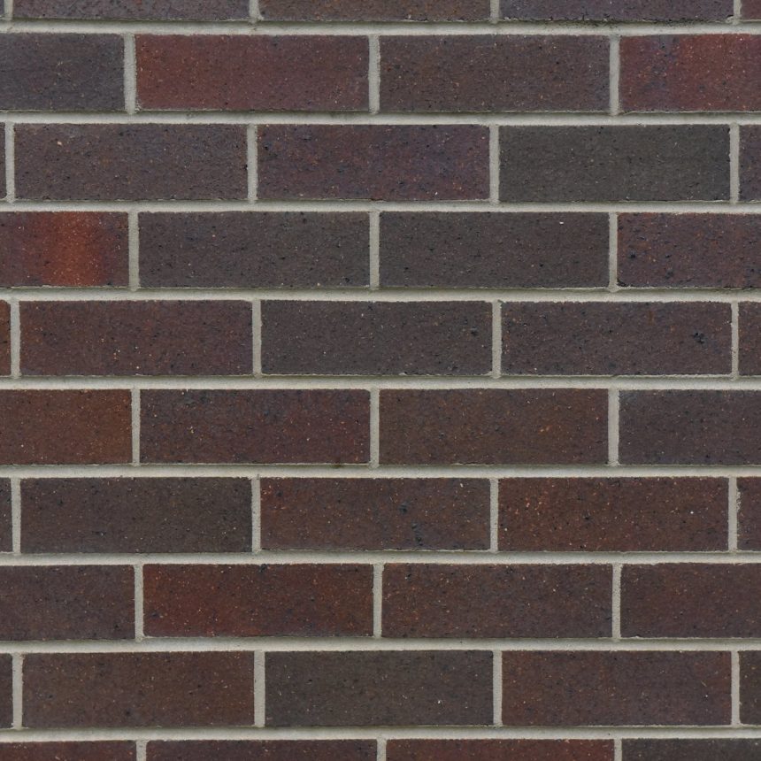 A close-up of a brick wall showcases evenly spaced, rectangular bricks in dark red, maroon, and brown hues. Subtle shades of the product Architectural Federation Blue peek through the thin, light-colored mortar that aligns the bricks in a horizontal pattern.