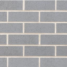 The gray brick wall, featuring a uniform grid-like pattern of horizontal and vertical lines, radiates a sleek elegance similar to that of Metallix Quartz. Its smooth texture is highlighted by light grout defining each perfectly aligned brick.