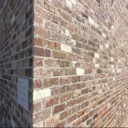 A close-up view of a corner where two walls made of Recycled Bricks Feature Grade. The bricks, which are irregularly shaped, display varying shades of red and brown with some white mortar visible. The image highlights the texture and details of the brickwork under natural light.