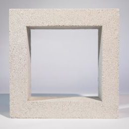 A Breeze Block Solid Grey, featuring a hollow center that resembles a frame, rests on a light-colored surface. Its rough and grainy texture contributes to its industrial appearance.