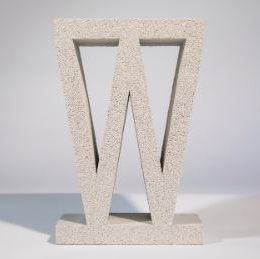 A large, textured stone sculpture of the letter W stands upright on a Breeze Block Solid Grey base against a neutral background.