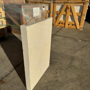A large Crema Novelda Sandblasted & Tumbled Drop Down tile stands upright on a concrete floor, with stacked wooden crates and wrapped pallets in the background.