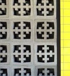 Close-up of a wall made from Breeze Block Cross Grey featuring a pattern of intersecting crosses, with a grey grid-patterned surface visible on the right side.