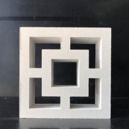 A Breeze Block Double Square Smooth White featuring intersecting geometric patterns stands out against a dark background, offering a symmetrical and open appearance.