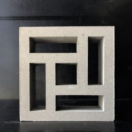 The Breeze Block Hindu Grey, featuring a geometric pattern of rectangular and square cutouts, stands upright against a dark background.