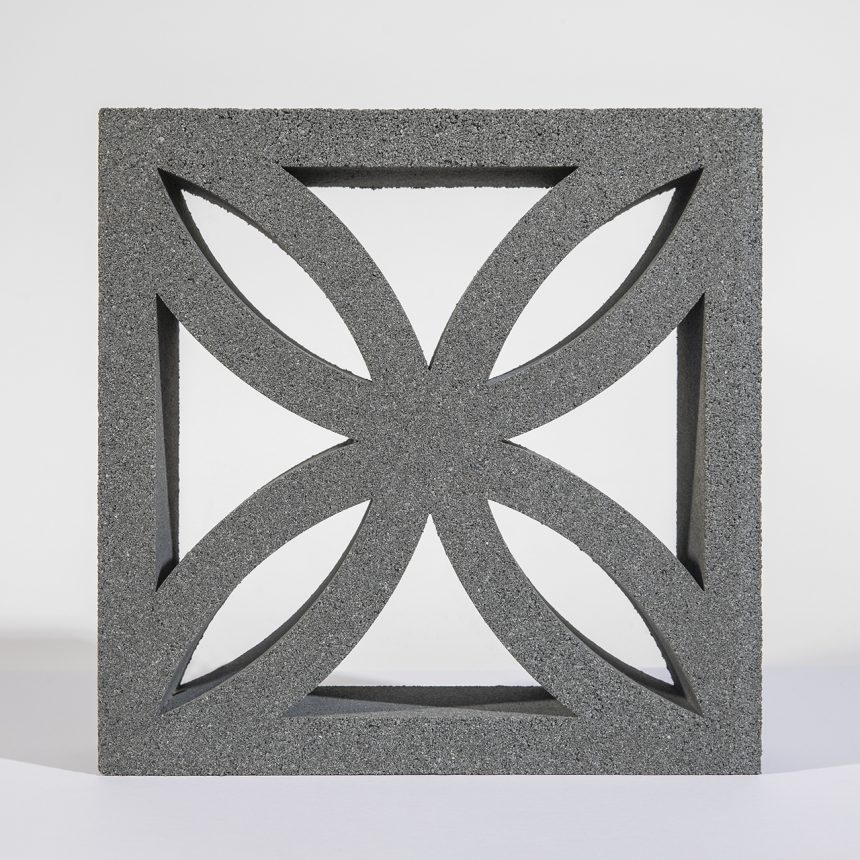 The Breeze Block Lotus Grey showcases a geometric design with four curved, pointed shapes arranged symmetrically within a square frame. Its textured surface creates a subtle shadow on the light background, enhancing its elegant appearance.