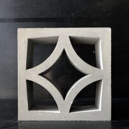 This decorative breeze block features a geometric cut-out design with four symmetrical curved shapes meeting at the centre, all set against a dark background.