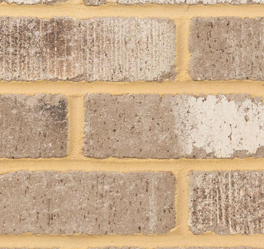 A close-up view of the Laneway Vibe Tumbled brick wall showcases its authentic charm, featuring alternating light and dark beige bricks with a rough texture. The light yellow-brown mortar complements the rustic appearance beautifully.
