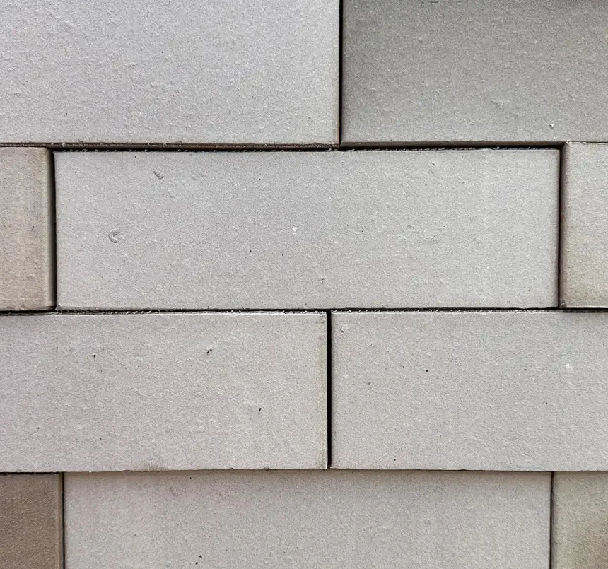 Close-up of a Merino brick wall featuring a neat, symmetrical pattern. The rectangular blocks are laid out in horizontal rows with subtle variations in warm grey shades, creating a textured look reminiscent of Merino wool's fine fibres.