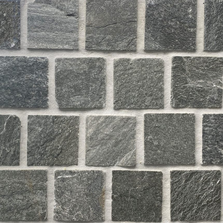 The wall features the Green Quartz Cobblestone Offset, with square green/ grey stone tiles showcasing a rough texture arranged in neat rows and columns. Subtle colour variations and natural patterns enhance its rustic appearance reminiscent of green quartz, while the cobblestone elements contribute an offset charm to the design.