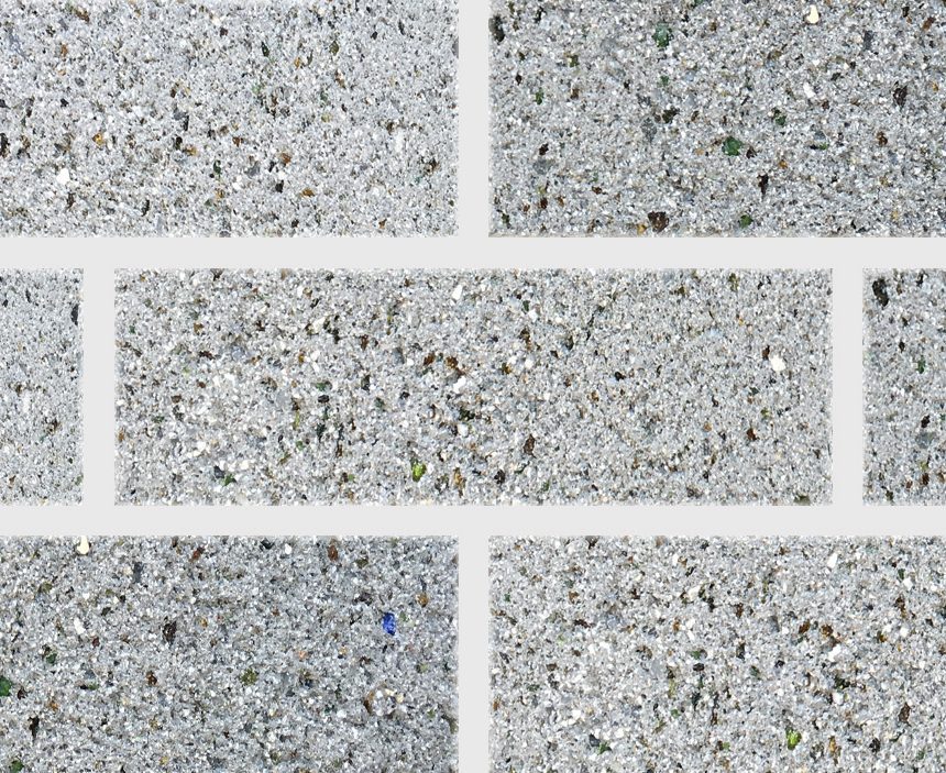 A close-up view of a wall tiled with Exposed Pewter ECO bricks arranged in a staggered pattern, showcasing their textured, grainy appearance with multicolored specks scattered throughout.