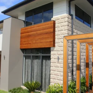 Modern two-story house with large windows, white and GB Sandstone Rockface Limestone exterior walls, wooden panel accents, and a wooden pergola in the landscaped front yard.