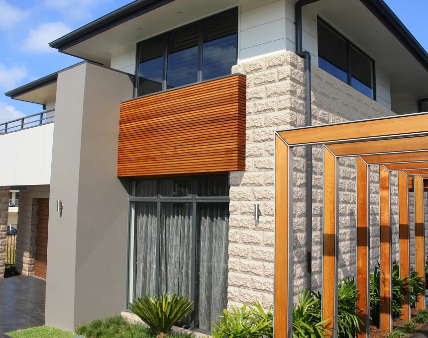 Modern two-story house with large windows, white and GB Sandstone Rockface Limestone exterior walls, wooden panel accents, and a wooden pergola in the landscaped front yard.