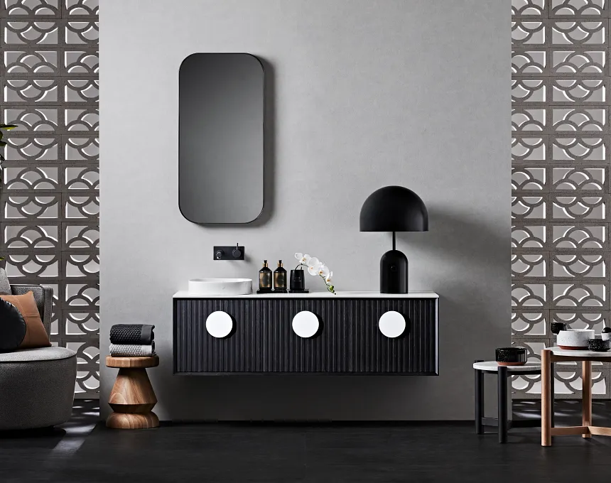Modern bathroom with GB Breeze Blocks Arc Pottery-inspired geometric wallpaper, a floating black vanity with large white circular handles, rectangular mirror, black lamp, and Arc Pottery decor with bottles and flowers on the counter.