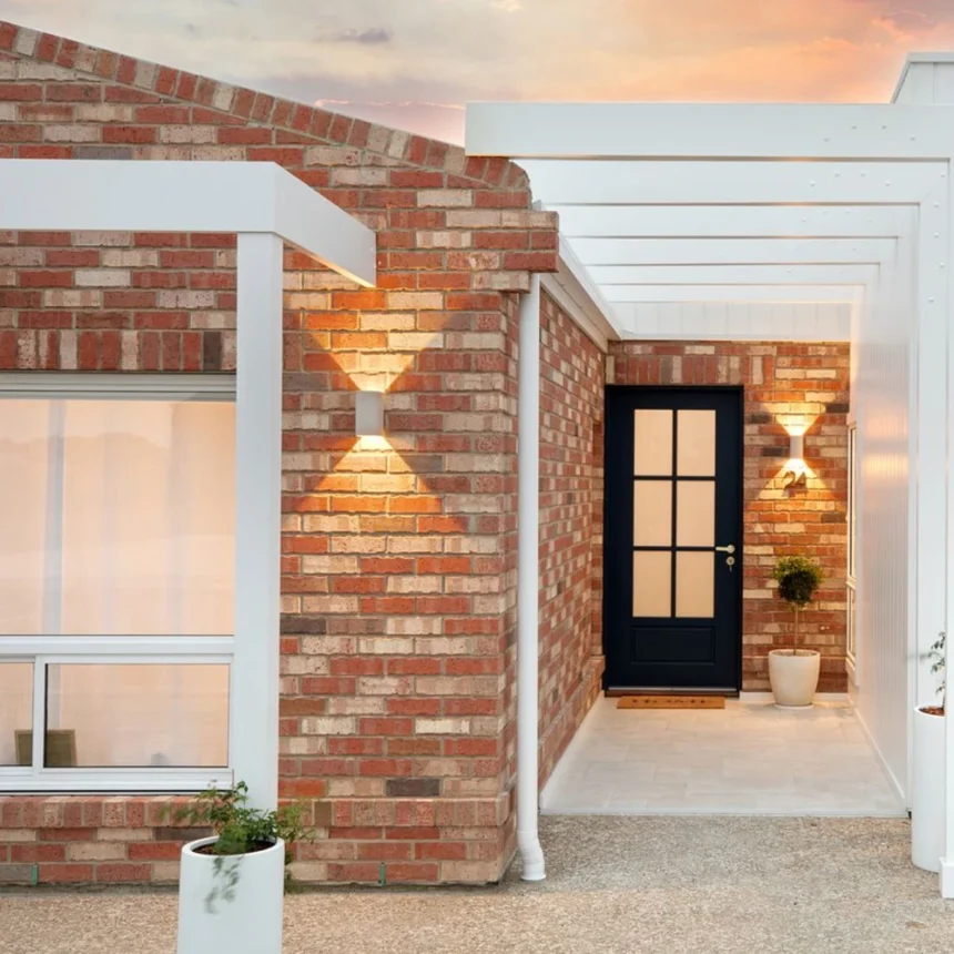 The entry way of a brick house using littlehampton McLaren Vale bricks which are a blend of red bricks, cream bricks and black bricks. The majority of the blend is red bricks and cream bricks. There is a white timber awning over the entry patheway to the front door. The front door is black with glass panels on the inside