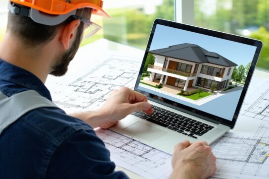 A person wearing a hard hat and safety vest works on a laptop displaying a 3D model of a house, with architectural blueprints spread out on the desk in front of them. Free estimating service