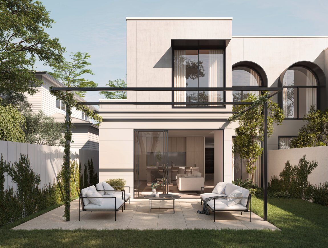Modern two-story house with large windows and minimalist fibre cement architecture, featuring a patio with white cushioned chairs, a glass table, and manicured lawn surrounded by greenery and a white fence.