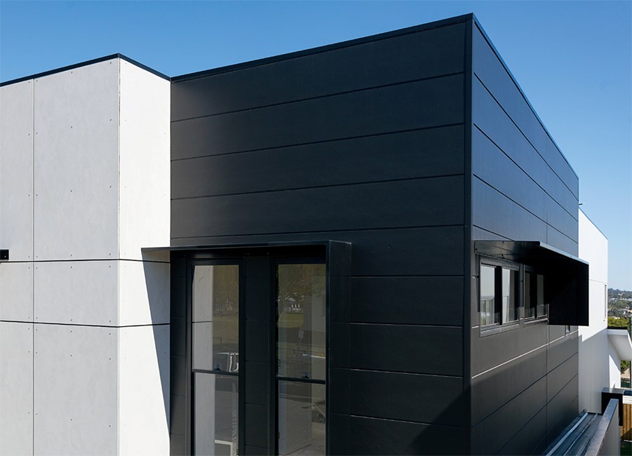 Modern building exterior featuring a combination of white and dark James Hardie Fibre Cement panels, flat rooflines, and large windows, set against a clear blue sky.