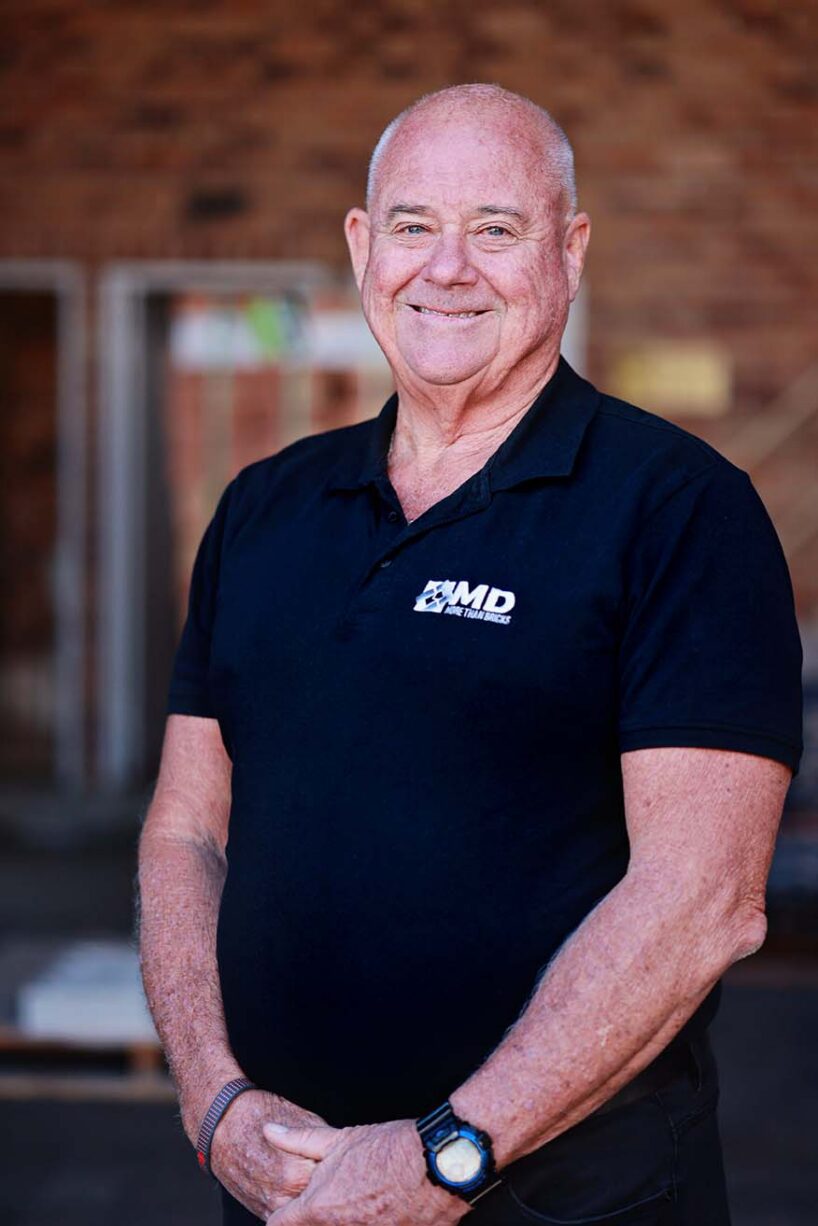 Mick Morley, a smiling middle-aged man in a black polo shirt with an MD More Than Bricks logo.